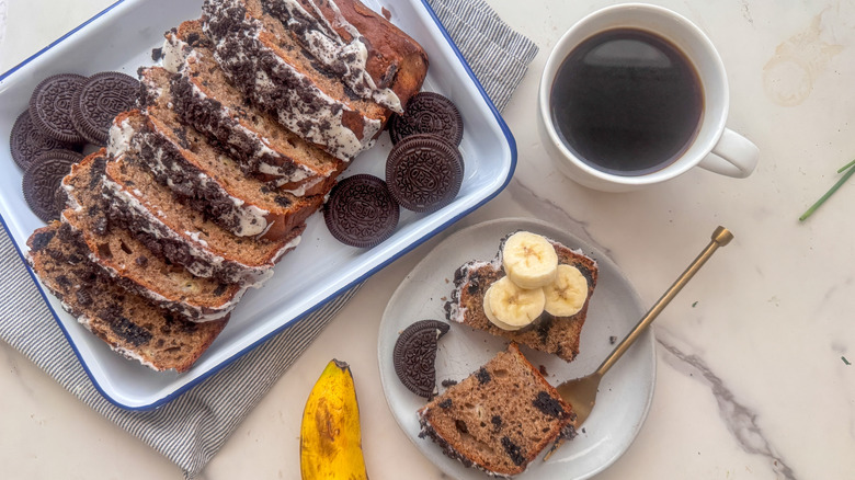 Sliced banana bread topped with crushed Oreos next to a cup of coffee