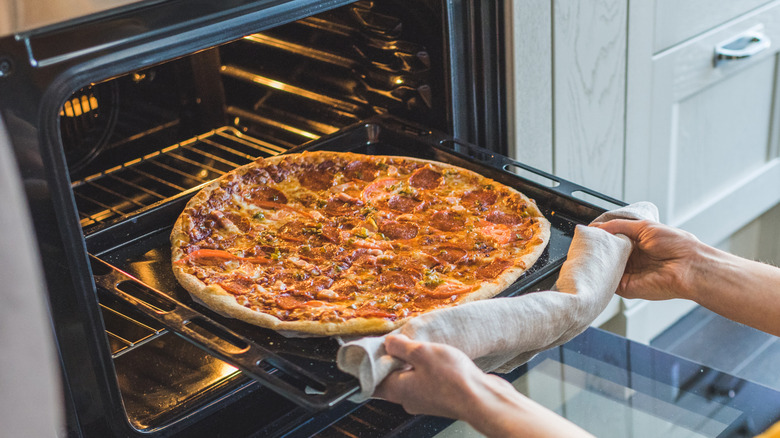 Someone placing a large thin crust pepperoni pizza into an oven
