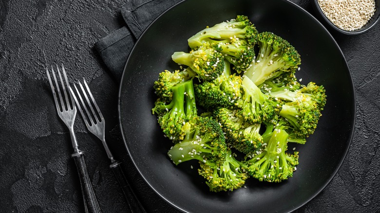 A plate of boiled broccoli and a small bowl of sesame seeds