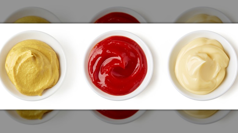 Dollops of tomato ketchup, yellow mustard, and mayonnaise in little jars