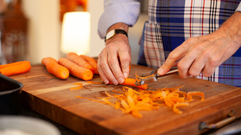 A person peeling carrots against a cutting board