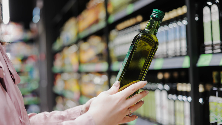 Someone picks up a bottle of olive oil at a store