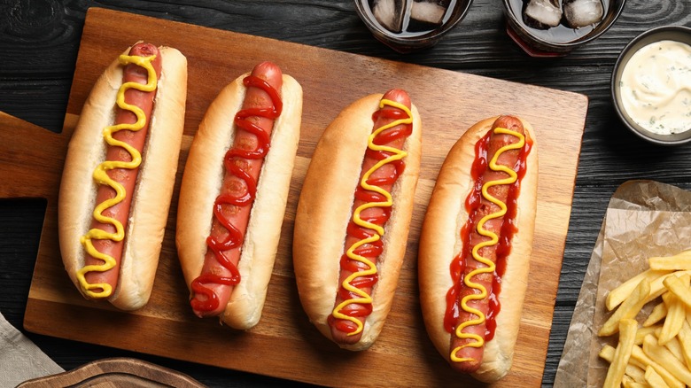 four hot dogs on a board topped with ketchup and mustard