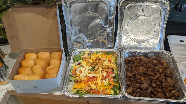 Large foil trays of Texas Roadhouse family sized dishes on kitchen counter
