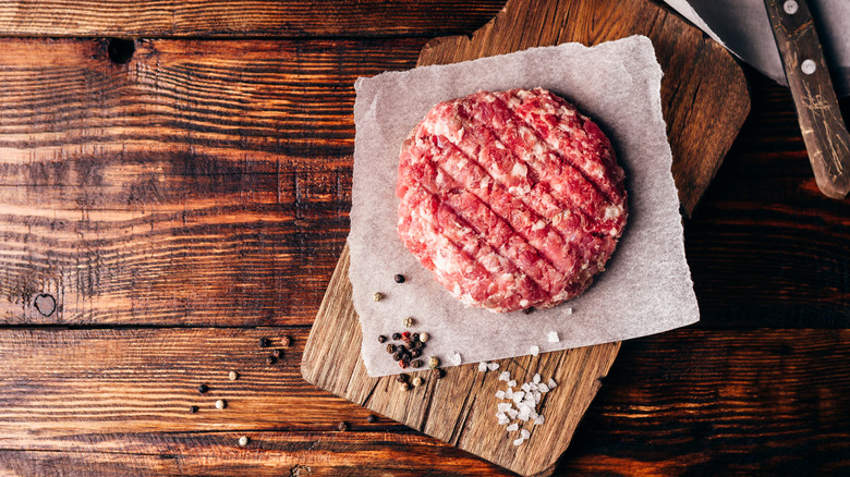 Burger patty on cutting board with salt and pepper