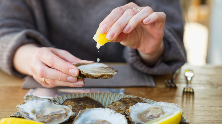 A person squeezes lemon on a raw oyster