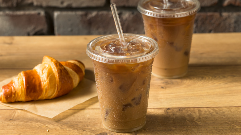 Two plastic cups filled with iced coffee with a croissant