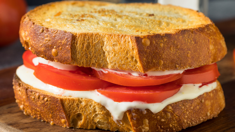 A toasted cheese and tomato sandwich on a cutting board.