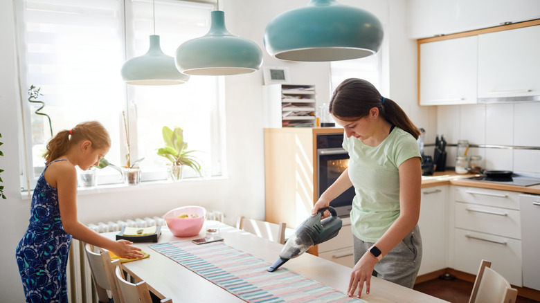 Woman using handheld vacuum cleaner for crumbs on kitchen table