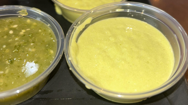 a small plastic cup of guacachile beside a cup of salsa verde