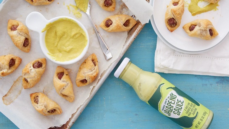 a flat lay of pigs in a blanket with a ramekin and bottle of Trader Joe's Jalapeño Sauce