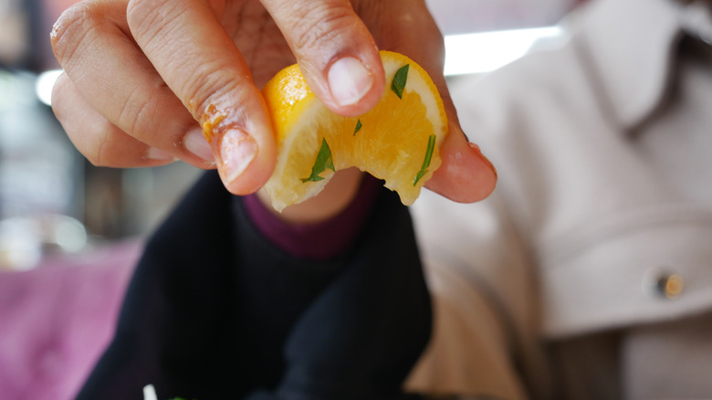 A hand is squeezing a wedge of lemon with herb stuck to it