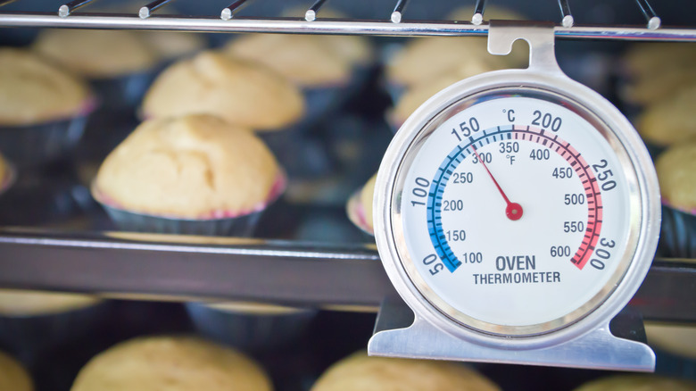 muffins baking behind a hanging oven thermometer