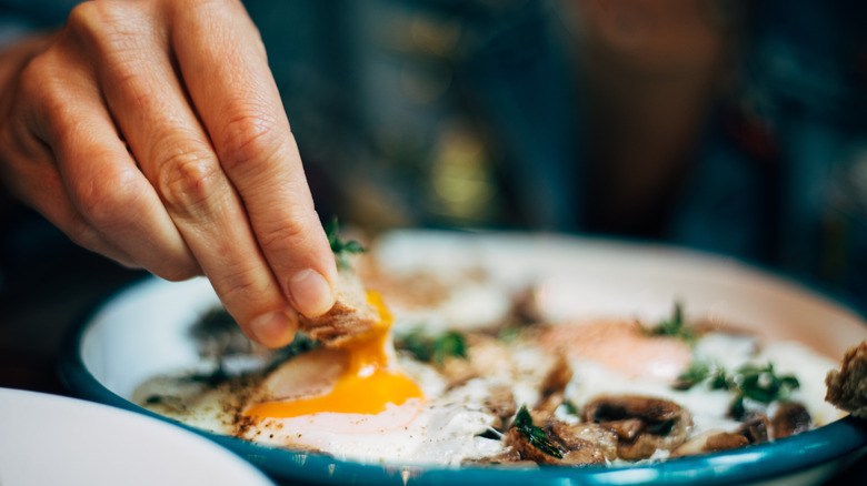Hand dipping bread into egg yolk on plate