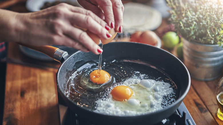 Hands cracking egg into pan on stove
