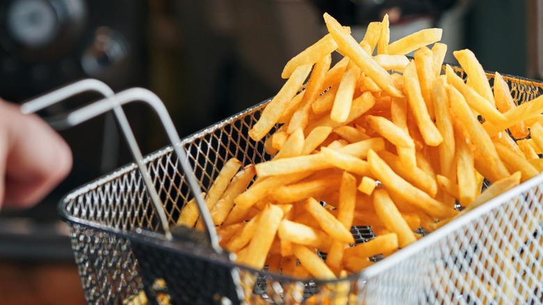 Crispy french fries being tossed inside of a frying basket in someone's kitchen
