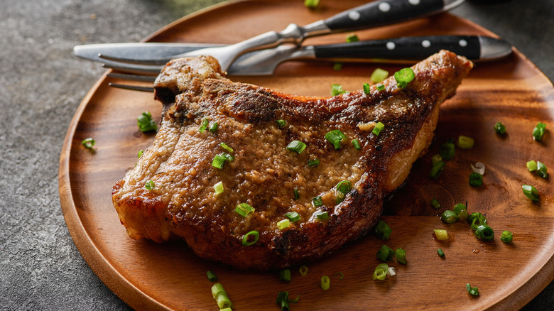 a seared pork chops with green onions on a wooden plate