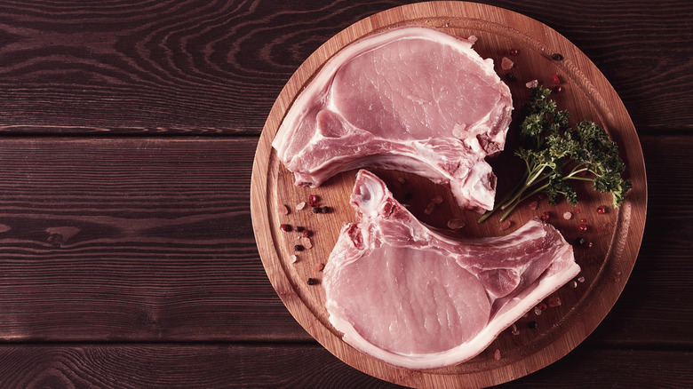 raw pork chops rest on a wooden board with herbs