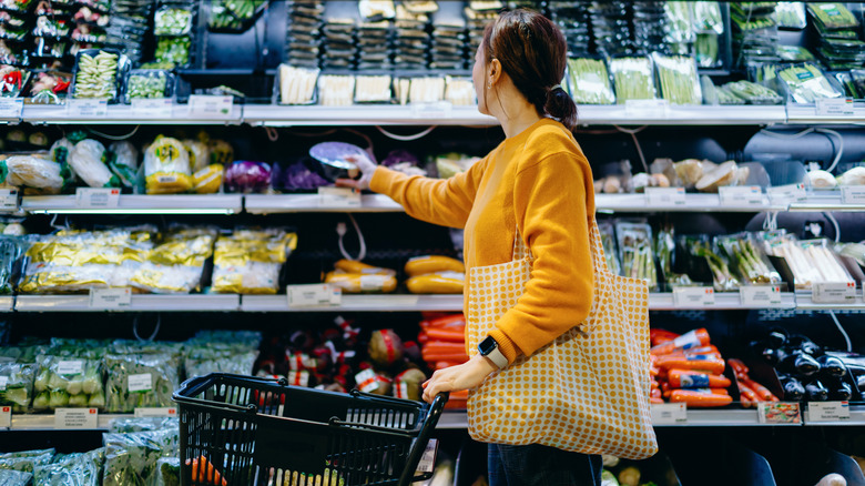 Shopper pushing cart in a grocery store and picking produce from the fridge