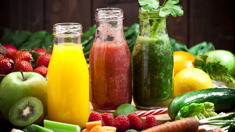 Three bottles of juice surrounded by fruits and veggies