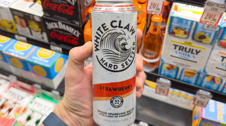 A person holds a white claw in front of a beer cooler