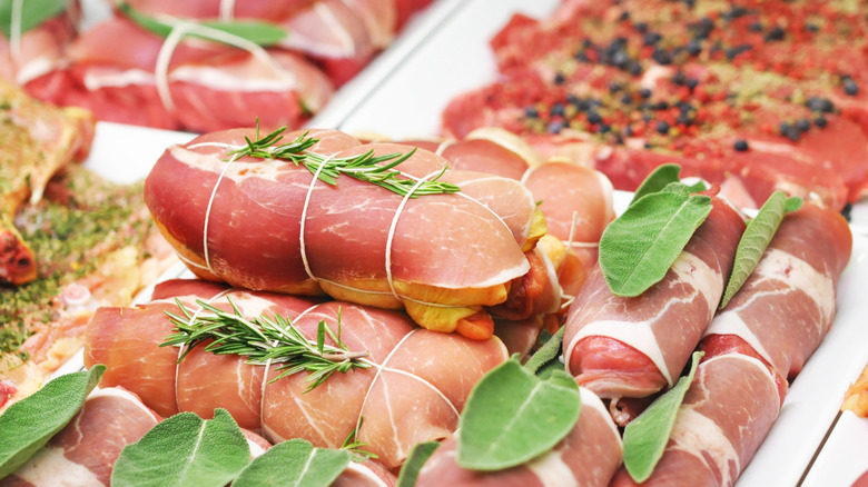 Rolls of Meat wrapped in twine and covered in herbs like sage and rosemary