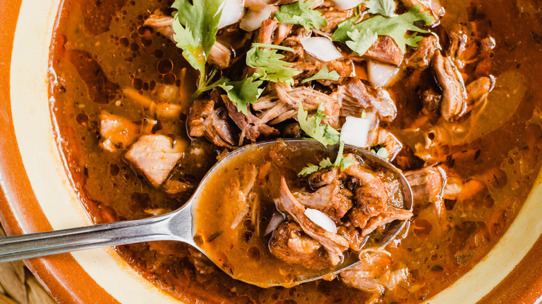A closeup of beef stew in an orange and white bowl with a metal spoon scooping up a spoonful of the stew to further illustrate the detailed spices and ingredients in the stew