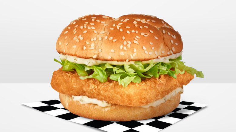 The Crispy Fish Sandwich from Checkers & Rally's sitting on a black and white checkered piece of butcher paper on a plain white background