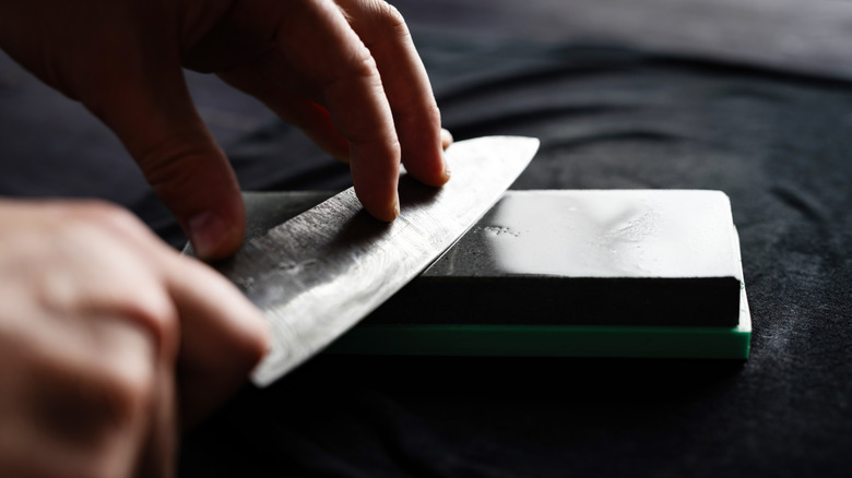 Person sharpening knife on whetstone.