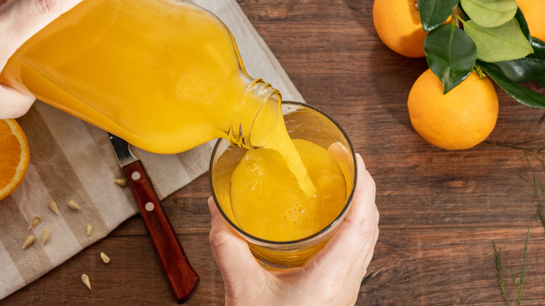 A person pours a glass of orange juice next to whole oranges
