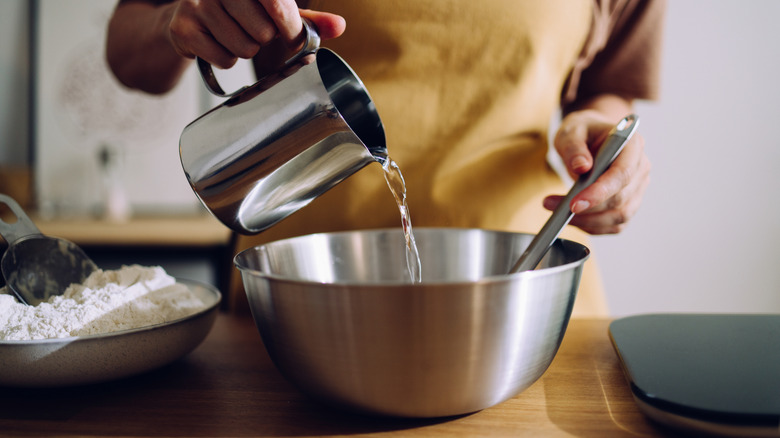 Person pouring water into dough