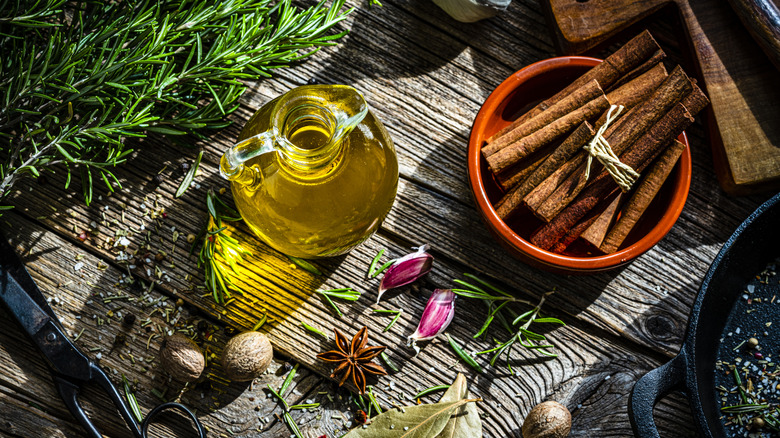 Glass container of olive oil surrounded by spices and herbs