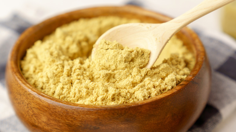 Mustard powder in wooden bowl with spoon on table
