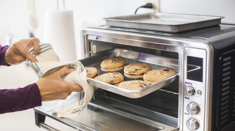 A person removing a tray of cookies from a toaster oven