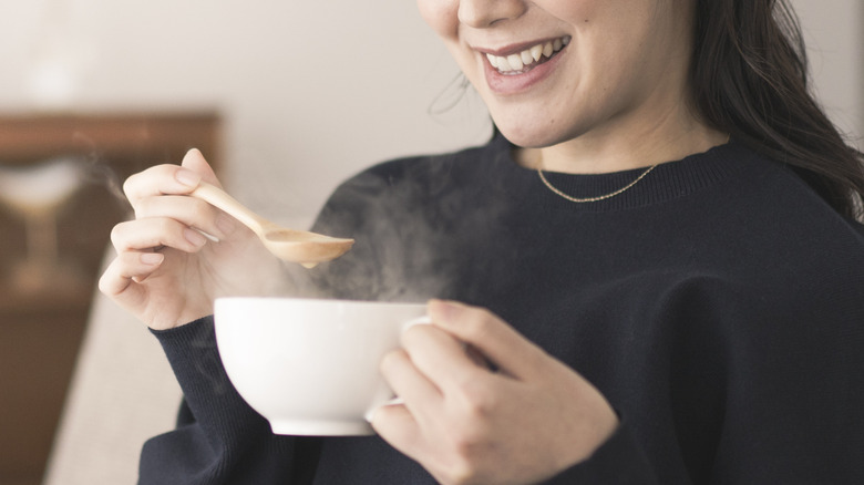 Person holding a white steaming bowl with a wooden spoon