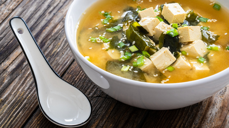 A bowl of miso soup with tofu, alongside a wide ceramic spoon