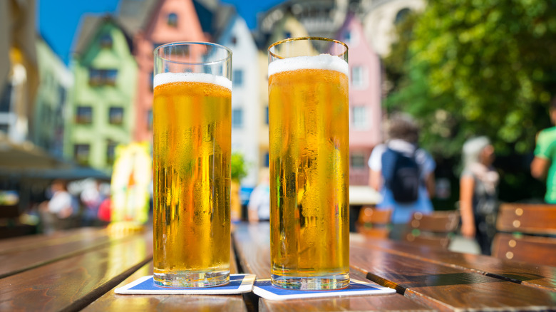 two tall thin glasses of kolsch on an outdoor wooden table on a sunny day