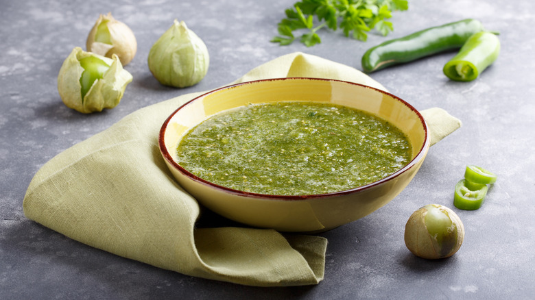A bowl of salsa verde next to ingredients