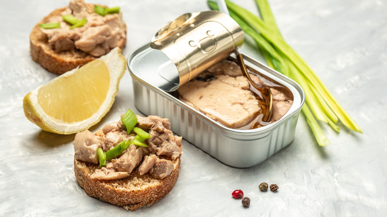 Cod liver tin with dressed crackers, a slice of lemon, peppercorns, and green onion