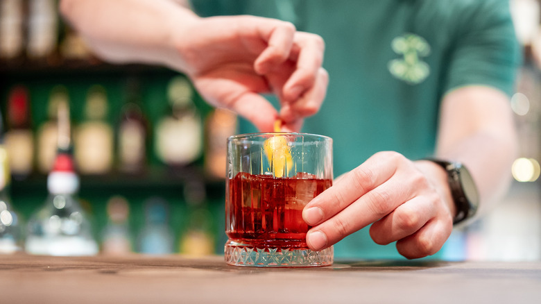 A person holding a cocktail while sliding a citrus peel along its edge