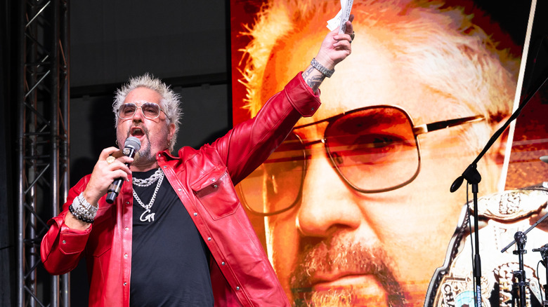 Chef and Food Network host Guy Fieri speaks into a microphone while addressing the crowd at a live event