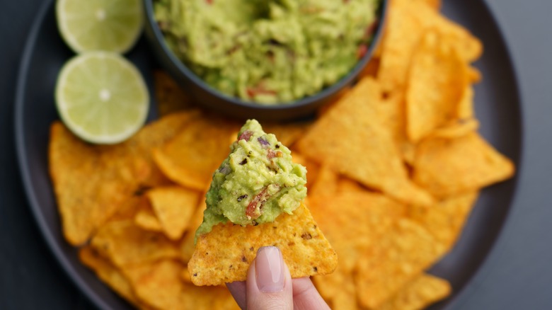 female hand holding a chip with guacamole