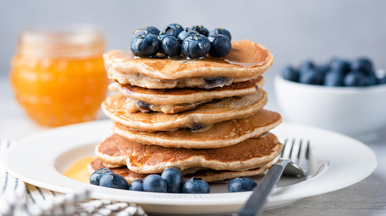 a stack of pancakes with blueberries on top with orange juice in the background