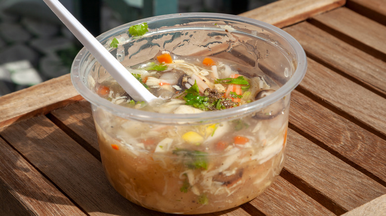 Atake away plastic container of soup sitting on a wooden table