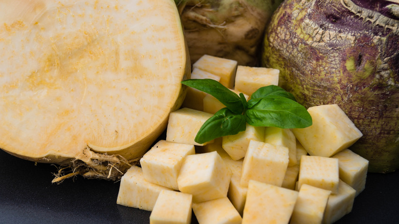 Chopped rutabaga next to a halved vegetable and a whole rutabaga