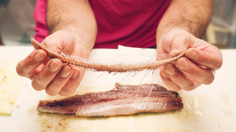 Hands holding a spine removed from a fish fillet on the counter below them