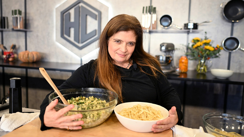 Alex Guarnaschelli stands by a counter with her arms around two bowls of pasta.