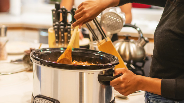 Woman stirs meat in a slow cooker