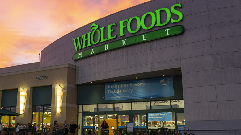 An illuminated Whole Foods Market sign on the exterior of a store at dusk