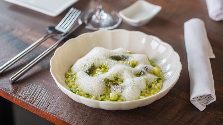 A plate of green risotto topped with a white foam